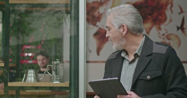 Kafe dükkanının önünde tablet tutan kendine güvenen girişimci. Mutlu bir kahve dükkanının portresi gülümseyen ve kendine güvenen sonuçlara bakıyor. Küçük işletme restoranı yerel sahibi