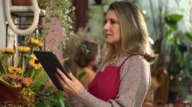 Çiçekçi dükkanının küçük bayan sahibi elinde tabletle envanteri kontrol ediyor.