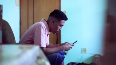 Young man using phone at home. Candid of a hispanic south american guy looking at smartphone screen