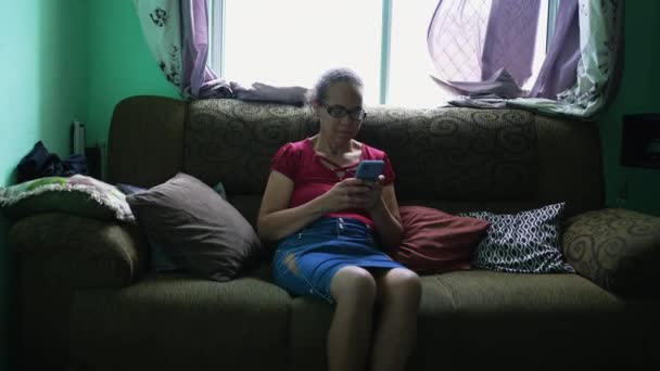 One Candid Hispanic Senior Woman Using Phone Home Sitting Couch — Vídeo de stock
