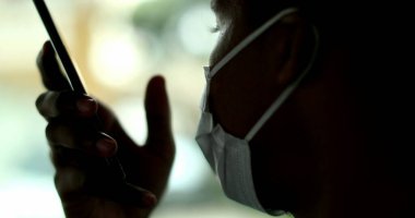 African person talking on cellphone device during pandemic wearing surgical mask in taxi car