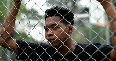 African mixed race man standing behind metal fence. Pensive black guy leaning body thinking
