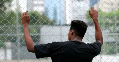 African black man leaning on metal fence outside watching game