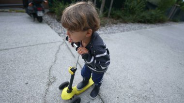 Child rides toy scooter outside
