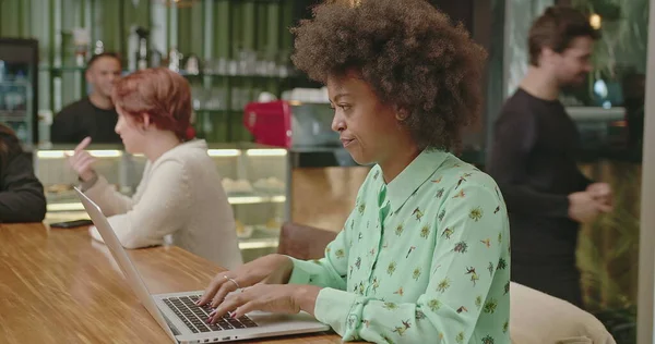 A happy black woman using laptop at coffee shop. One African American girl typing on computer keyboard smiling. A female entrepreneur person looking at laptop screen