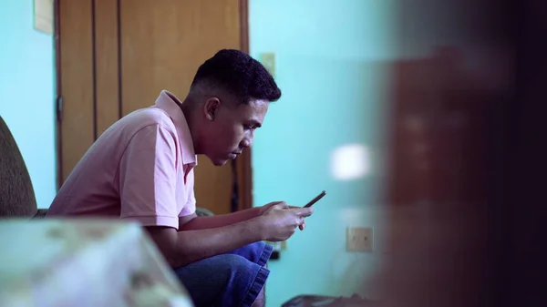 Young man using phone at home. Candid of a hispanic south american guy looking at smartphone screen