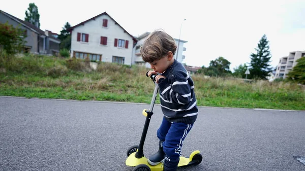 Little boy riding three wheeled scooter outdoors