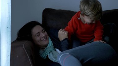 Toddler jumping on mother lying on sofa. Child jumps on top of mom in slow-motion