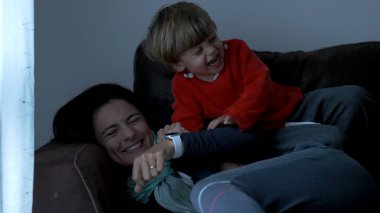 Toddler jumping on mother lying on sofa. Child jumps on top of mom in slow-motion