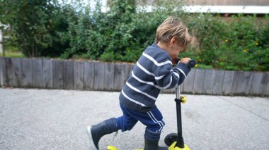 Little boy riding three wheeled scooter outdoors