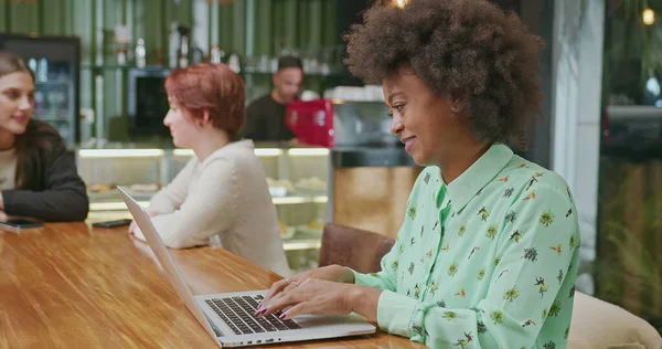 A happy black woman using laptop at coffee shop. One African American girl typing on computer keyboard smiling. A female entrepreneur person looking at laptop screen