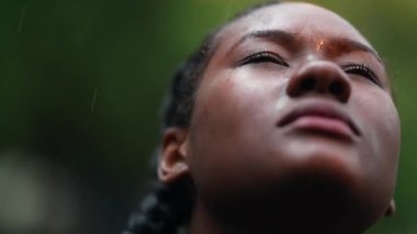 Yağmur altında Afrikalı genç bir kadın. Siyah etnik kökenli kız yağmur yağarken gökyüzüne bakıyor