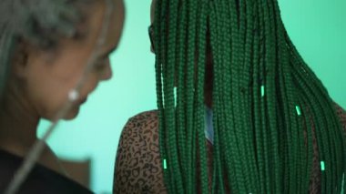 Two young black latina women showing their braided hair. Hispanic girls with cool box braids green hairstyle
