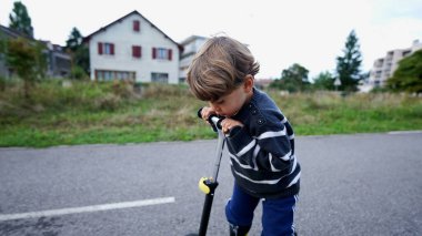 Little boy riding three wheeled scooter outdoors