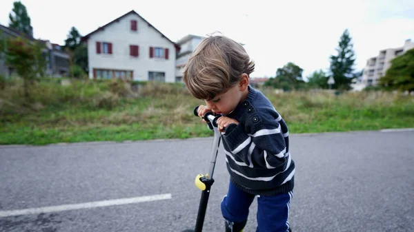 Little boy riding three wheeled scooter outdoors