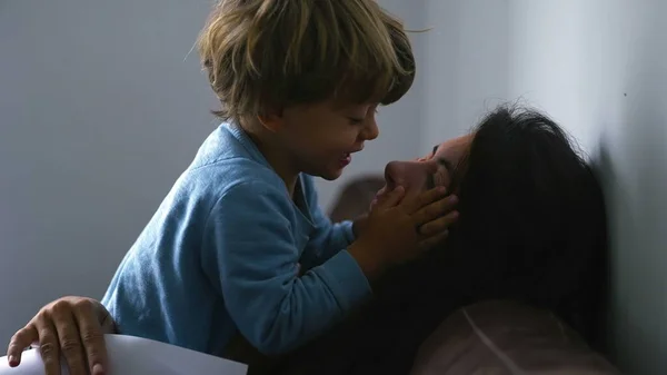 Little boy biting mother nose, real life authentic family moment at home