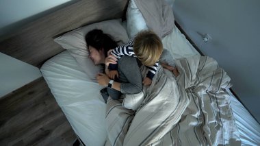 Mother and child in bed in the morning. kid jumping on top of parent lying in bed