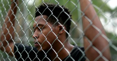 Pensive black guy leaning on security metal fence