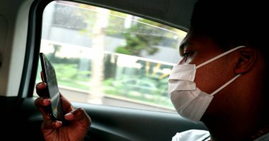 Black man in taxi browsing internet on smartphone device wearing pandemic mask