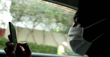 Black African man looking at cellphone inside car wearing surgical mask