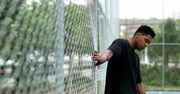 Black guy at basketball court holding into metal fence posing