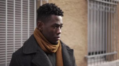 Pensive black man standing outside in city downtown. Thoughtful African guy waiting