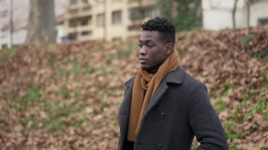 Pensive black man standing outside in cold winter season wearing scar and coat