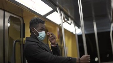 African man adjusting face mask while commuting on train holding bar handrail