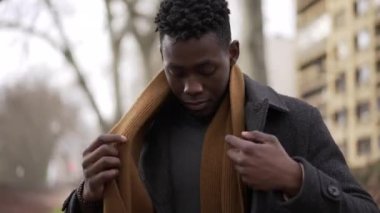 Black man putting scarf outdoors in winter season. African guy adjusting scaf in the cold wearing coat