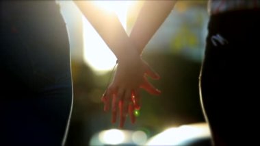 Lesbian couple joining hands outside in nature with lens-flare