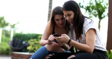 Girlfriends using smartphone device. Women checking cellphone