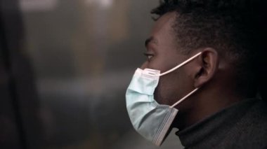 Metro metrosunun içinde siyah bir adam. Pencereden dışarı bakıyor. Yüz maskesi takıyor.