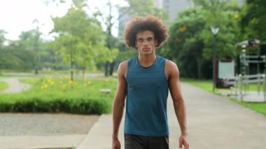 Afrikalı adam kameraya bakarak parkta yürüyor.