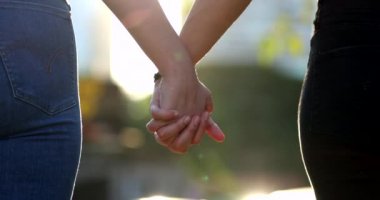 Arka planda güneş ışığının parlamasıyla birleşen ellerin yakın çekimi. İki aşık arasındaki güzel romantik an