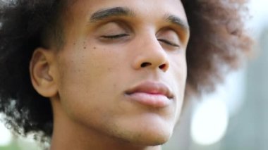 Young black man with eyes closed outside