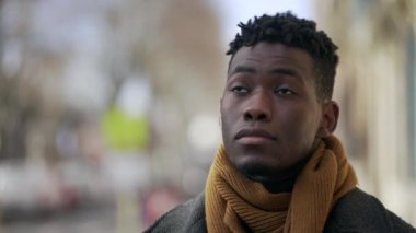 Thoughtful black man standing outside close-up face portrait in city tracking shot during winter
