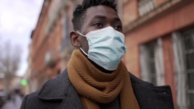 Siyah Afrikalı adam şehir kaldırımında cerrahi maske takıyor.