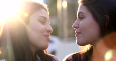 Girlfriends kissing outside in the sunlight. Candid gay women kiss