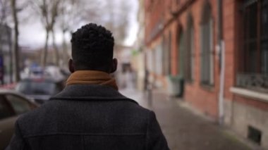 Black man walking outdoors in city sidewalk during winter. back of African person in downtown