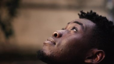 Düşünceli siyah adam gülümseyen gökyüzüne bakıyor.