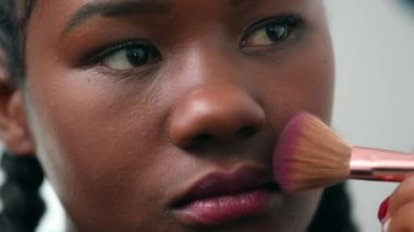 Siyah kız makyaj pudrası sürüyor. Afrikalı genç bir kadın aynaya bakıyor