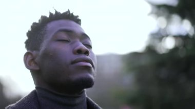 Genç siyah adam meditasyon ve tefekkür için gözlerini kapayıp açıyor. Afrikalı derin bir nefes alıyor.