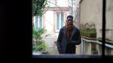 Young black man stepping outside walking through corridor, person opening door
