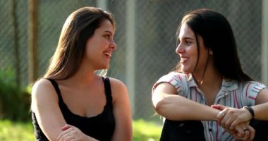 Parkta öylesine sohbet eden iki kız arkadaş, gülümseyen ve gülen genç kadınlar.