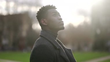 African young black man standing at park looking up in contemplation