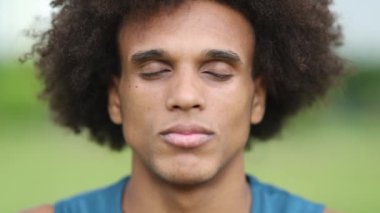 Genç Afrikalı adam gözlerini kapatıyor derin bir nefes alıyor ve gözlerini açıyor mutlu bir şekilde gülümsüyor.