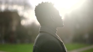 Mutlu siyah Afrikalı adam kameraya gülümsüyor açık havada dalgın dalgın dikiliyor.