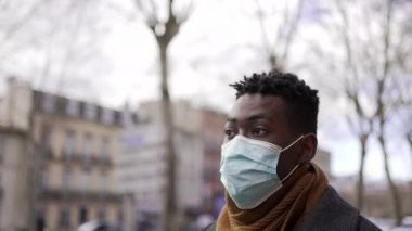 Siyahi adam salgın sırasında dışarıda yürüyor. Ameliyat maskesi takıyor.
