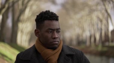 Düşünceli bir adam kış boyunca parkta palto ve eşarp giyerek yürüyor.