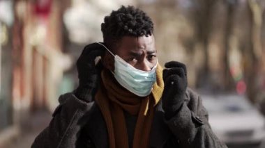 Siyah adam kış mevsiminde şehir dışında yürürken mavi maske takıyor.